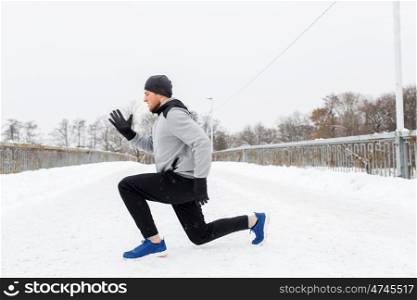 fitness, sport, people, exercising and healthy lifestyle concept - young man doing squats and warming up on snow covered winter bridge