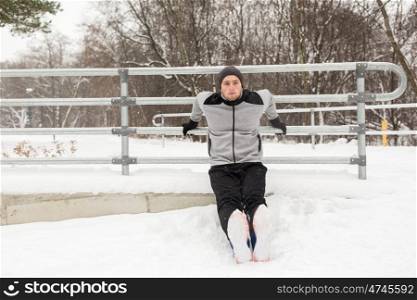 fitness, sport, people, exercising and healthy lifestyle concept - young man doing triceps dips and warming up at fence in winter