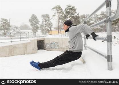 fitness, sport, people, exercising and healthy lifestyle concept - young man doing triceps dips and warming up at fence in winter