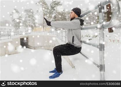 fitness, sport, people, exercising and healthy lifestyle concept - young man doing squats and warmig up at fence in winter. sports man doing squats at fence in winter