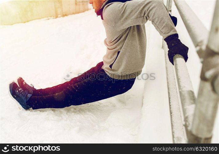 fitness, sport, people, exercising and healthy lifestyle concept - young man doing triceps dips and warming up at fence in winter. sports man doing triceps dips at fence in winter