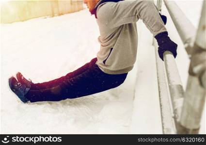 fitness, sport, people, exercising and healthy lifestyle concept - young man doing triceps dips and warming up at fence in winter. sports man doing triceps dips at fence in winter