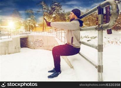 fitness, sport, people, exercising and healthy lifestyle concept - young man doing squats and warmig up at fence in winter. sports man doing squats at fence in winter