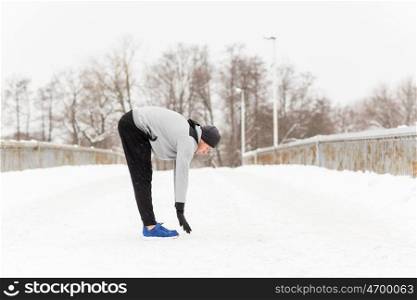 fitness, sport, people, exercising and healthy lifestyle concept - young man stretching leg and warming up on snow covered winter bridge