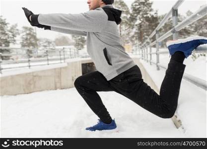 fitness, sport, people, exercising and healthy lifestyle concept - young man stretching leg and warming up at fence in winter