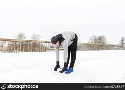 fitness, sport, people, exercising and healthy lifestyle concept - young man stretching leg and warming up on snow covered winter bridge