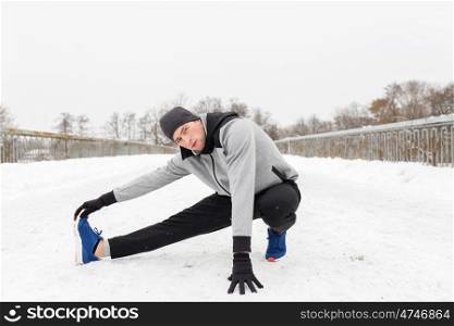 fitness, sport, people, exercising and healthy lifestyle concept - young man stretching leg and warmig up on snow covered winter bridge