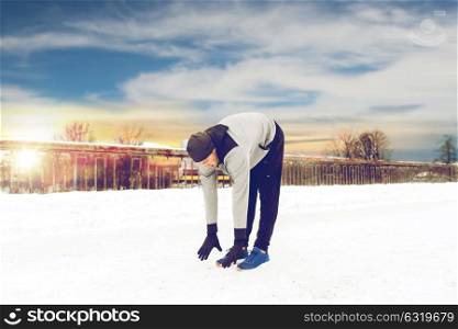 fitness, sport, people, exercising and healthy lifestyle concept - young man stretching leg and warming up on snow covered winter bridge. man exercising and stretching leg on winter bridge