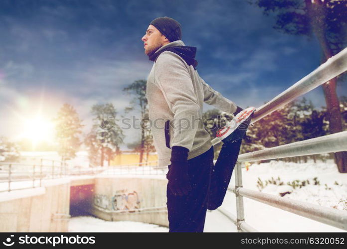 fitness, sport, people, exercising and healthy lifestyle concept - young man stretching leg and warming up at fence in winter. sports man stretching leg at fence in winter