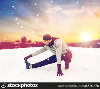 fitness, sport, people, exercising and healthy lifestyle concept - young man stretching leg and warmig up on snow covered winter bridge. man exercising and stretching leg on winter bridge
