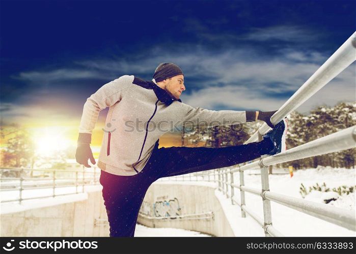 fitness, sport, people, exercising and healthy lifestyle concept - young man stretching leg and warming up at fence in winter. sports man stretching leg at fence in winter