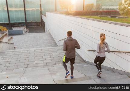 fitness, sport, people, exercising and lifestyle concept - couple running downstairs on city stairs