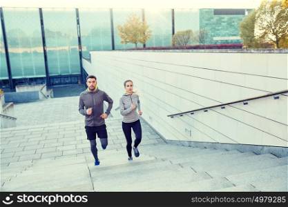 fitness, sport, people, exercising and lifestyle concept - happy couple running upstairs on city stairs. happy couple running upstairs on city stairs