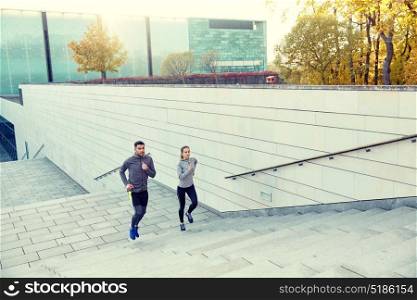 fitness, sport, people, exercising and lifestyle concept - happy couple running upstairs on city stairs. happy couple running upstairs on city stairs