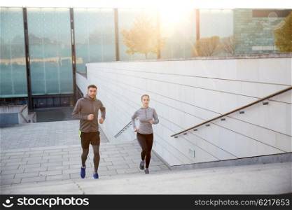 fitness, sport, people, exercising and lifestyle concept - happy couple running upstairs on city stairs