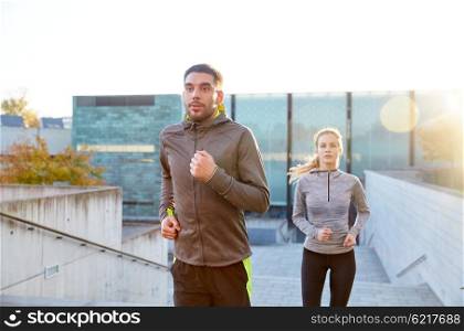 fitness, sport, people, exercising and lifestyle concept - happy couple running upstairs on city stairs
