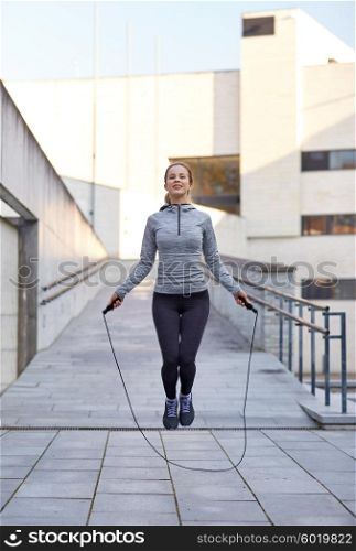 fitness, sport, people, exercising and lifestyle concept - happy woman skipping with jump rope outdoors