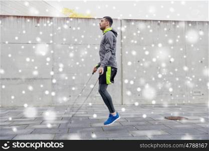 fitness, sport, people, exercising and lifestyle concept - man skipping with jump rope outdoors over snow