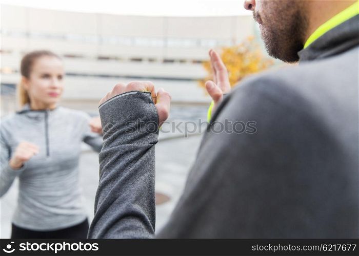 fitness, sport, people, exercising and martial arts concept - close up of woman with trainer working out self defense strike on city street