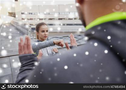 fitness, sport, people, exercising and martial arts concept - young woman with trainer working out self defense strike on city street over snow