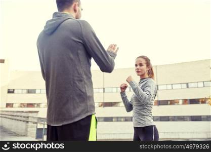 fitness, sport, people, exercising and martial arts concept - young woman with trainer working out self defense strike on city street. woman with trainer working out self defense strike