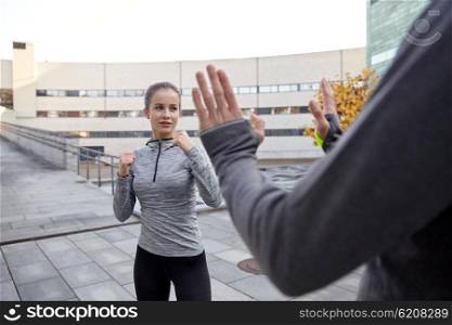 fitness, sport, people, exercising and martial arts concept - young woman with trainer working out self defense strike on city street