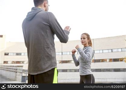 fitness, sport, people, exercising and martial arts concept - young woman with trainer working out self defense strike on city street