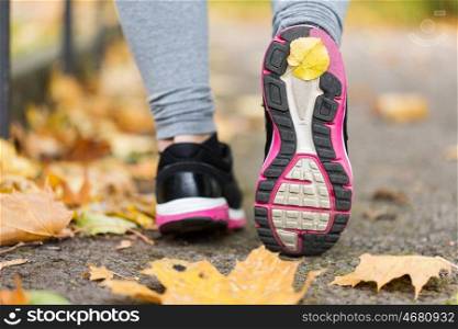 fitness, sport, people, footwear and healthy lifestyle concept - close up of young woman running in sneakers at autumn park