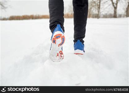 fitness, sport, people, footwear and healthy lifestyle concept - close up of male feet running along winter road and snow