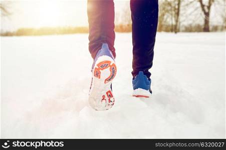 fitness, sport, people, footwear and healthy lifestyle concept - close up of male feet running along winter road and snow. close up of feet running along snowy winter road