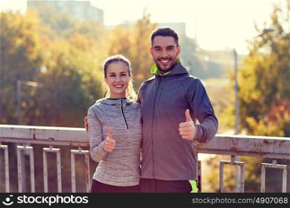 fitness, sport, people, gesture and lifestyle concept - smiling couple outdoors showing thumbs up at city. smiling couple showing thumbs up outdoors