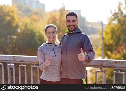 fitness, sport, people, gesture and lifestyle concept - smiling couple outdoors showing thumbs up at city