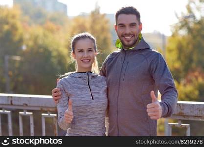fitness, sport, people, gesture and lifestyle concept - smiling couple outdoors showing thumbs up at city