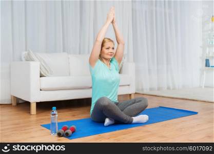 fitness, sport, people, meditation and yoga concept - woman meditating in lotus pose on mat at home