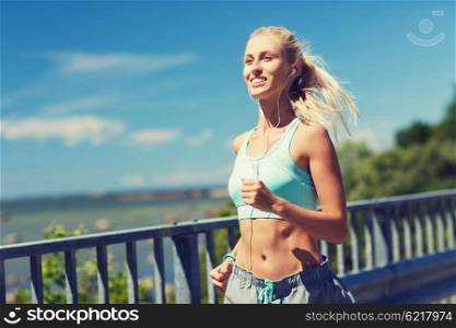 fitness, sport, people, music and healthy lifestyle concept - smiling young woman with earphones running outdoors