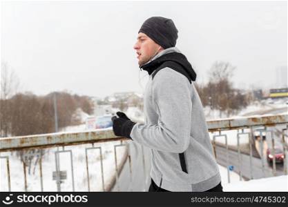 fitness, sport, people, music and healthy lifestyle concept - young man in earphones running along winter bridge
