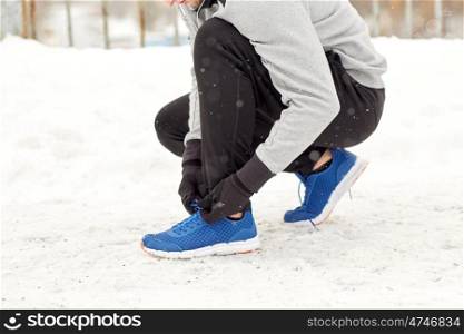 fitness, sport, people, music and healthy lifestyle concept - young man in earphones tying shoe on winter bridge