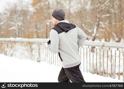 fitness, sport, people, music and healthy lifestyle concept - young man in earphones running along snow covered winter bridge