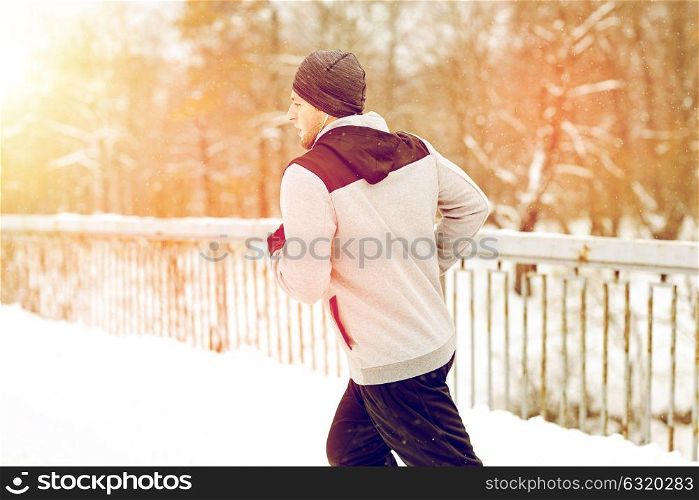 fitness, sport, people, music and healthy lifestyle concept - young man in earphones running along snow covered winter bridge. man in earphones running along winter bridge