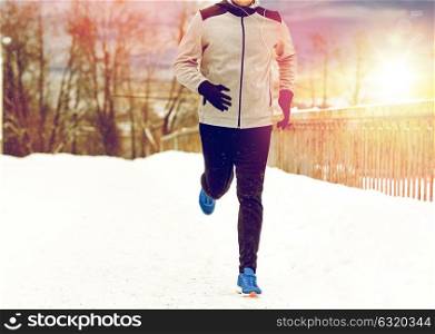 fitness, sport, people, music and healthy lifestyle concept - young man in earphones running along snow covered winter bridge. man in earphones running along winter bridge
