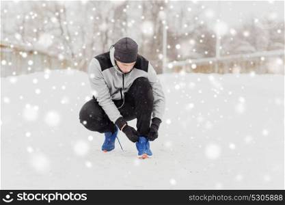 fitness, sport, people, music and healthy lifestyle concept - young man man in earphones tying shoe on winter bridge. man with earphones tying sports shoe in winter