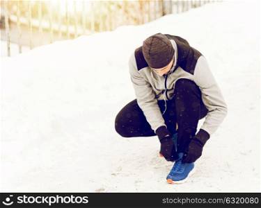 fitness, sport, people, music and healthy lifestyle concept - young man man in earphones tying shoe on winter bridge. man with earphones tying sports shoe in winter