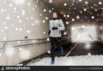 fitness, sport, people, season and healthy lifestyle concept - happy young man running along pedestrian subway tunnel in winter. happy man running along subway tunnel in winter