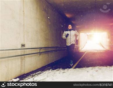 fitness, sport, people, season and healthy lifestyle concept - happy young man running along pedestrian subway tunnel in winter. happy man running along subway tunnel in winter