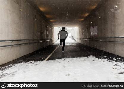 fitness, sport, people, season and healthy lifestyle concept - young man running along pedestrian subway tunnel in winter