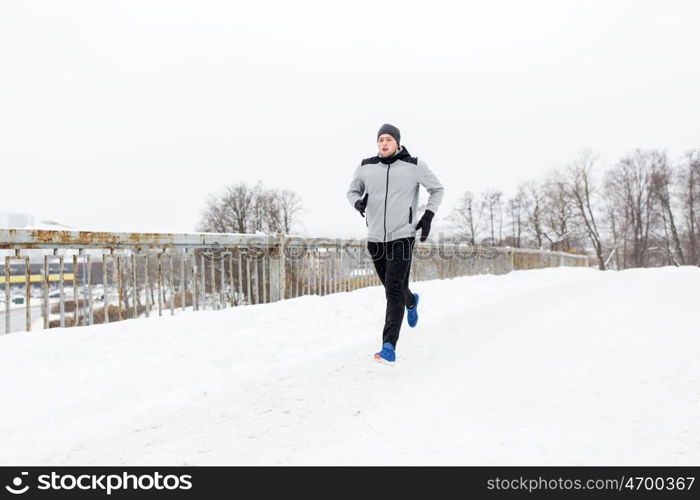 fitness, sport, people, season and healthy lifestyle concept - young man running along snow covered winter bridge road