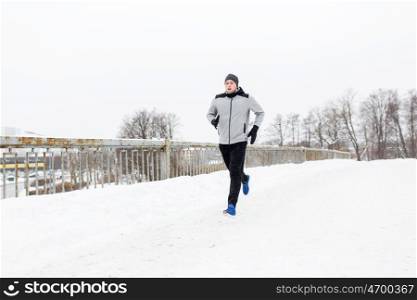 fitness, sport, people, season and healthy lifestyle concept - young man running along snow covered winter bridge road
