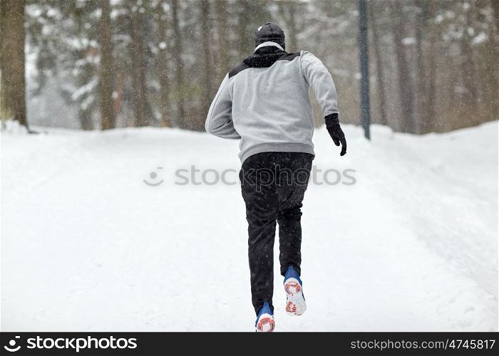 fitness, sport, people, season and healthy lifestyle concept - young man running on snow covered winter road in forest (motion blurred picture)