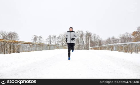 fitness, sport, people, season and healthy lifestyle concept - young man running along snow covered winter bridge road