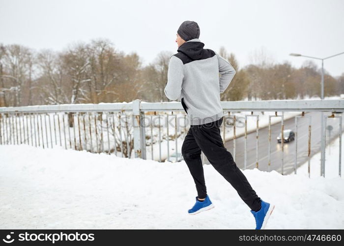 fitness, sport, people, season and healthy lifestyle concept - young man running along snow covered winter bridge road